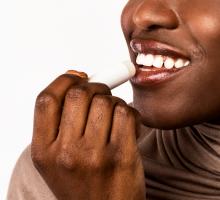 Black woman applying lip balm against a white background